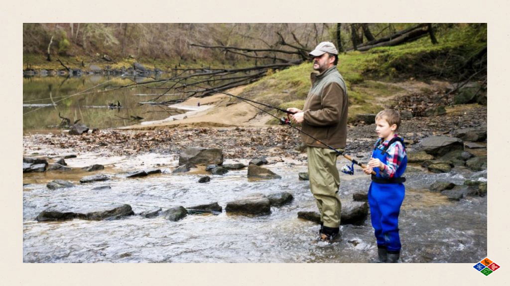 A photograph of an adult and a child standing in a river, fishing.