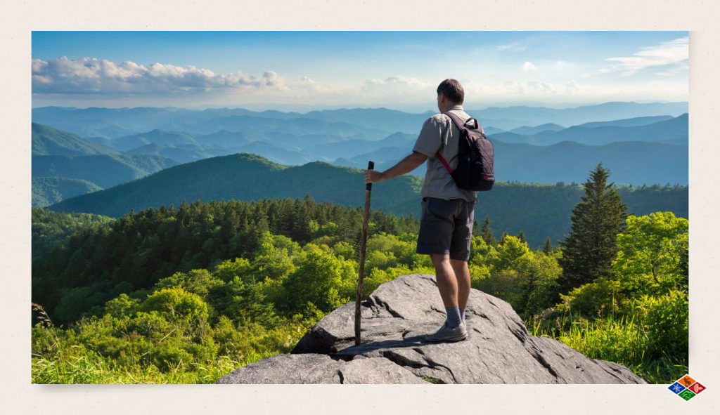 A person with a hiking stick stands on a trail in the Smoky Mountains.