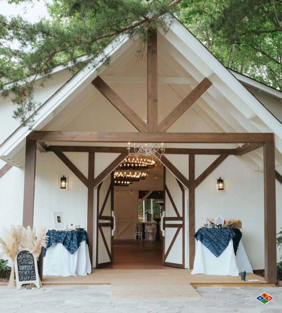 The white reception barn at Bluff Mountain Inn, timber trusses framing open doors and chandeliers glowing inside