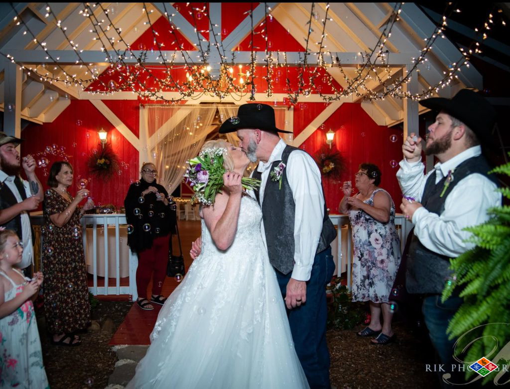 Newlyweds kissing under string lights in front of the red barn at Bluff Mountain Inn as guests blow bubbles
