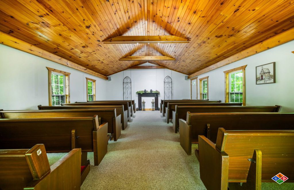 Inside the white chapel at Bluff Mountain Inn, with wooden pews, a pine plank vaulted ceiling and windows onto the woods