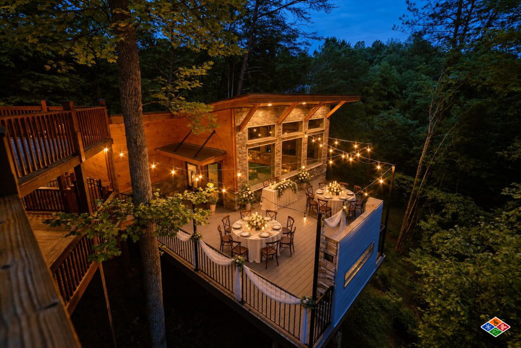 Silvercreek pool house deck at dusk set with round reception tables, white florals, draped railings and string lights