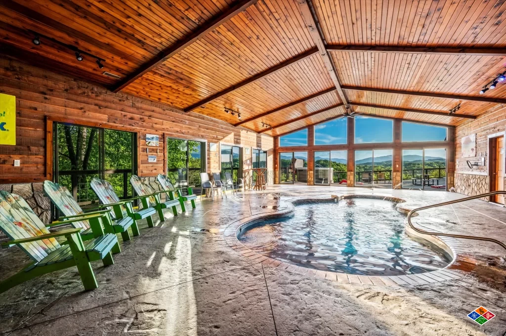 The indoor heated pool at Mountain View Mansion beneath a vaulted wood ceiling, with a wall of windows looking out to the Smoky Mountains